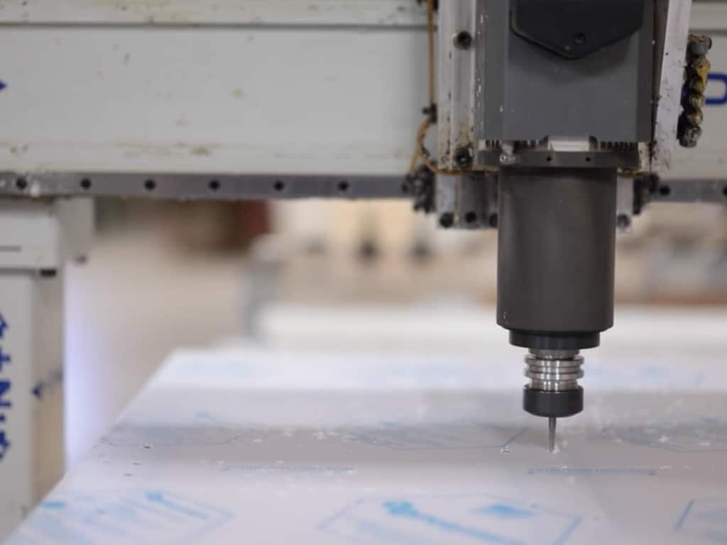 Close-up of a CNC machine with a drill bit carving a flat sheet of material. The scene conveys precision and industrial efficiency.