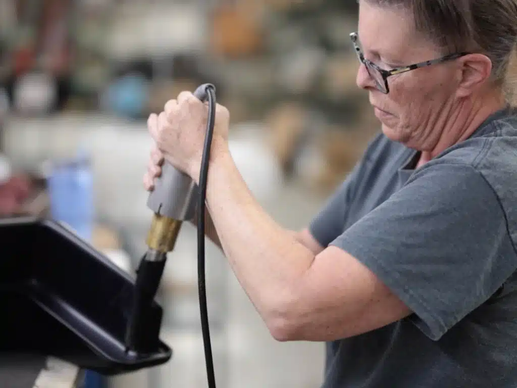 A person wearing glasses focuses on using a heat gun in a workshop, conveying concentration and skill in a hands-on work environment.
